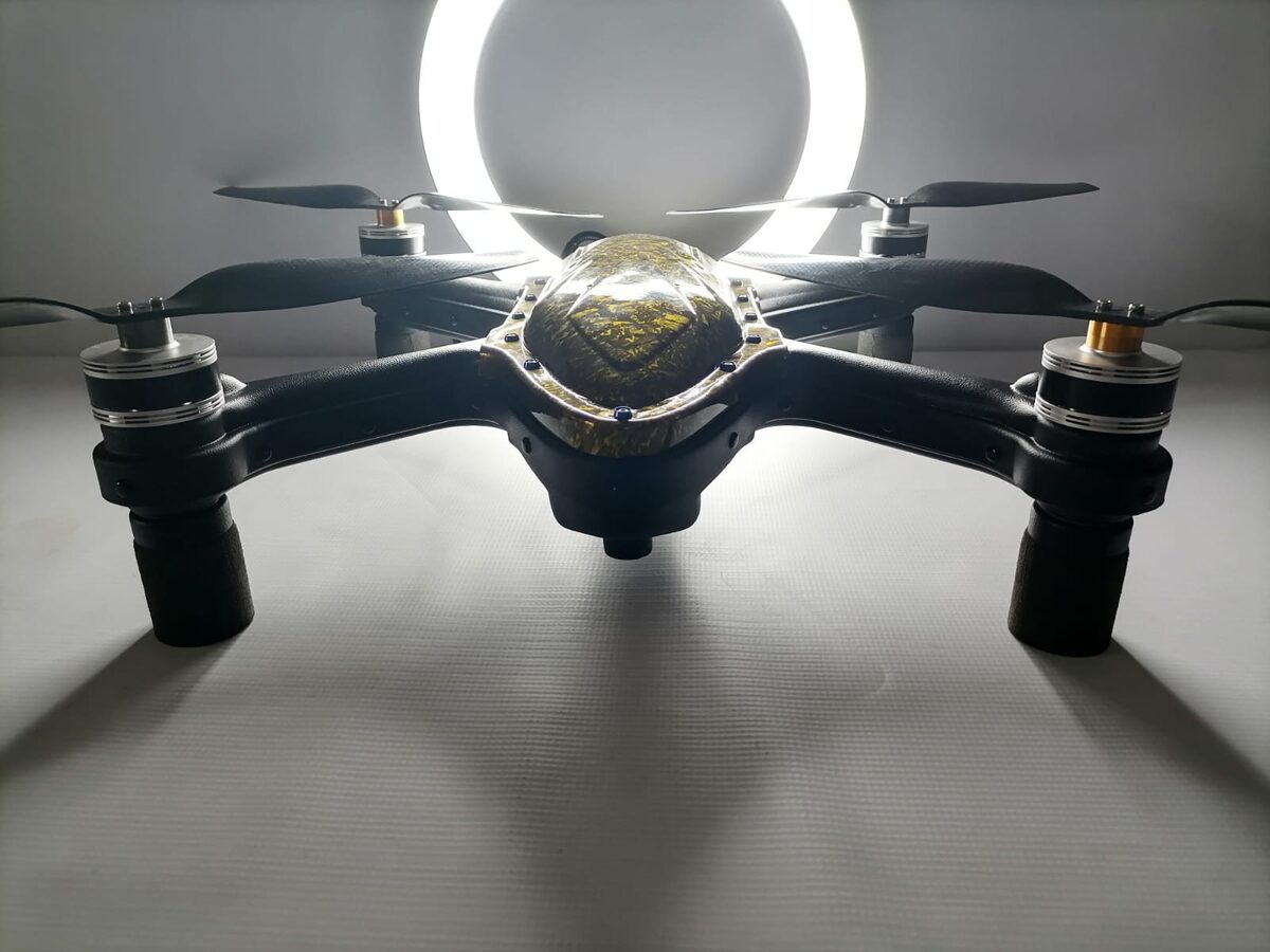 Cuta Copter Trident V2 BOSS Edition quadcopter, front view, with a gold carbon-pattern canopy, four large propellers, and foam landing legs